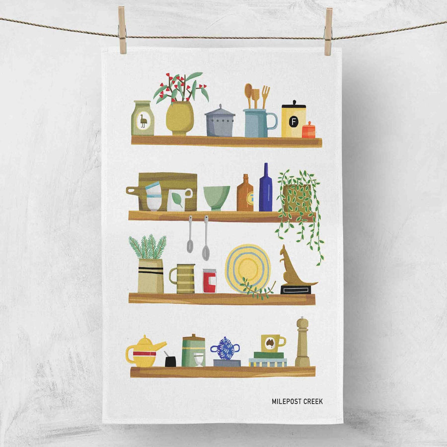 Illustrated kitchen scene on a white linen tea towel with 'Milepost Creek' branding.