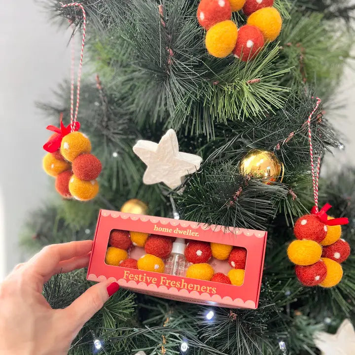 Festive freshener packaging held in front of a Christmas tree with decorations.