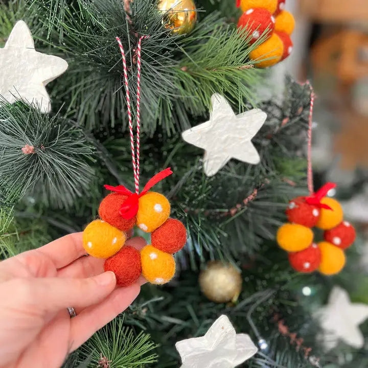 Colorful felt ball ornaments held in front of a decorated Christmas tree.