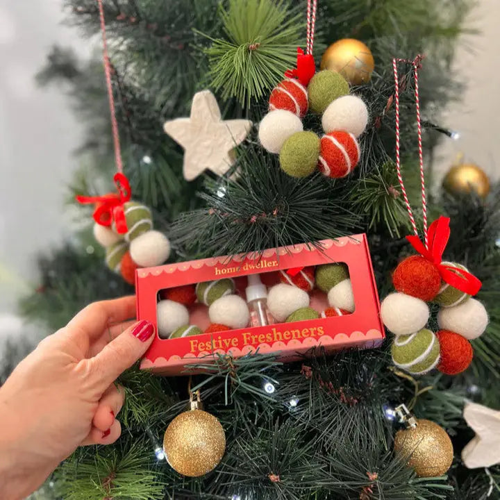 Hand holding a box of 'Festive Fresheners' in front of a decorated Christmas tree.