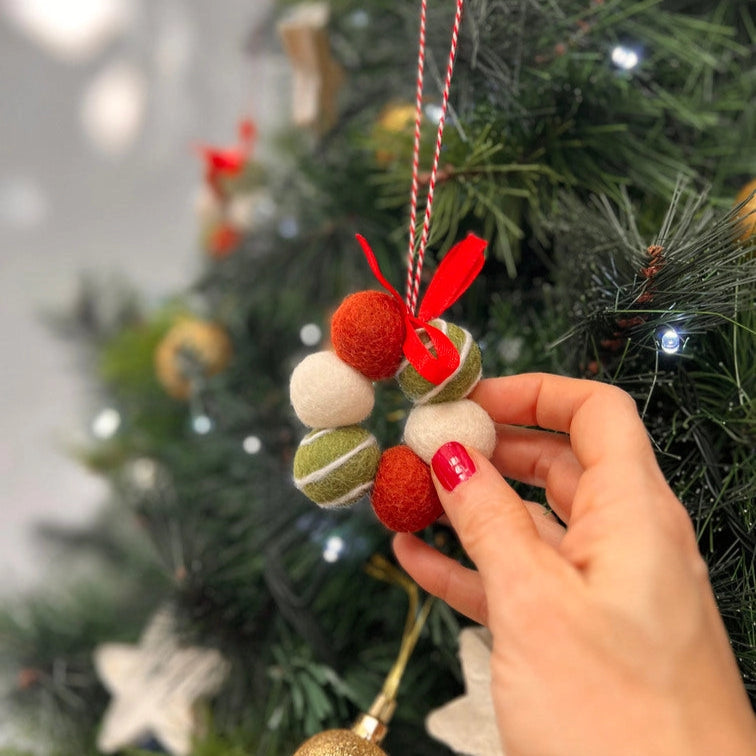 Hand holding a decorative ornament with red and green elements against a Christmas tree background