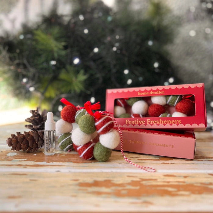 Festive freshener with red and white decorations on a wooden surface with a blurred Christmas tree background.