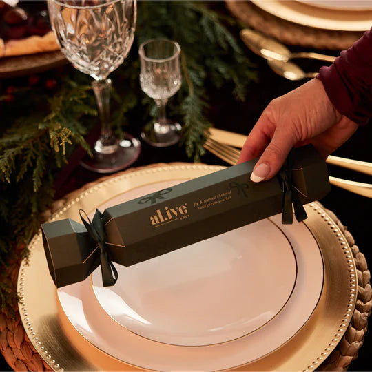 Hand holding a wrapped gift labeled 'alive' on a festive table setting with plates and glasses.