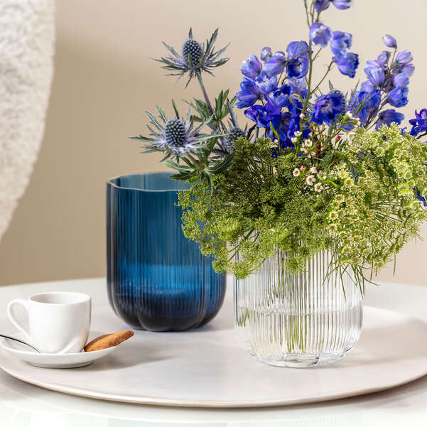 Two vases, one blue and one clear, with a bouquet of flowers on a table.