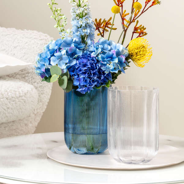 Blue vase with flowers on a table next to a clear vase