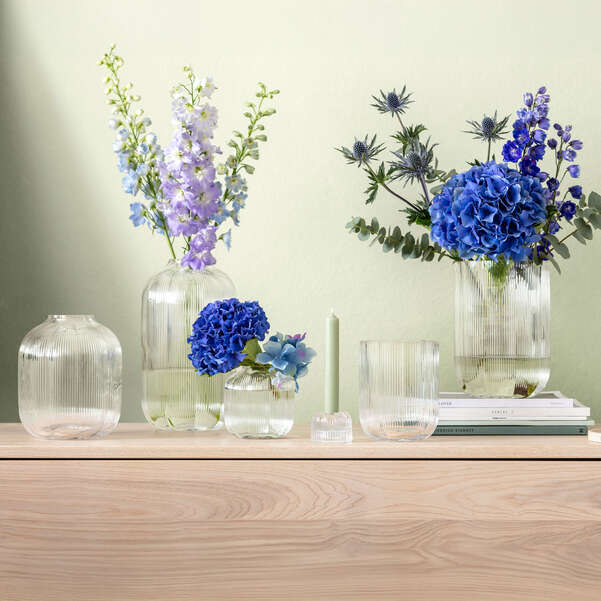 Decorative setup with vases, flowers, and candles on a wooden surface against a light green wall.