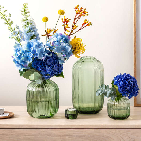 Three green glass vases with floral arrangements on a wooden surface.
