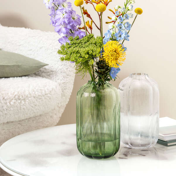 Green ribbed vase with colorful flowers on a table next to a white couch.
