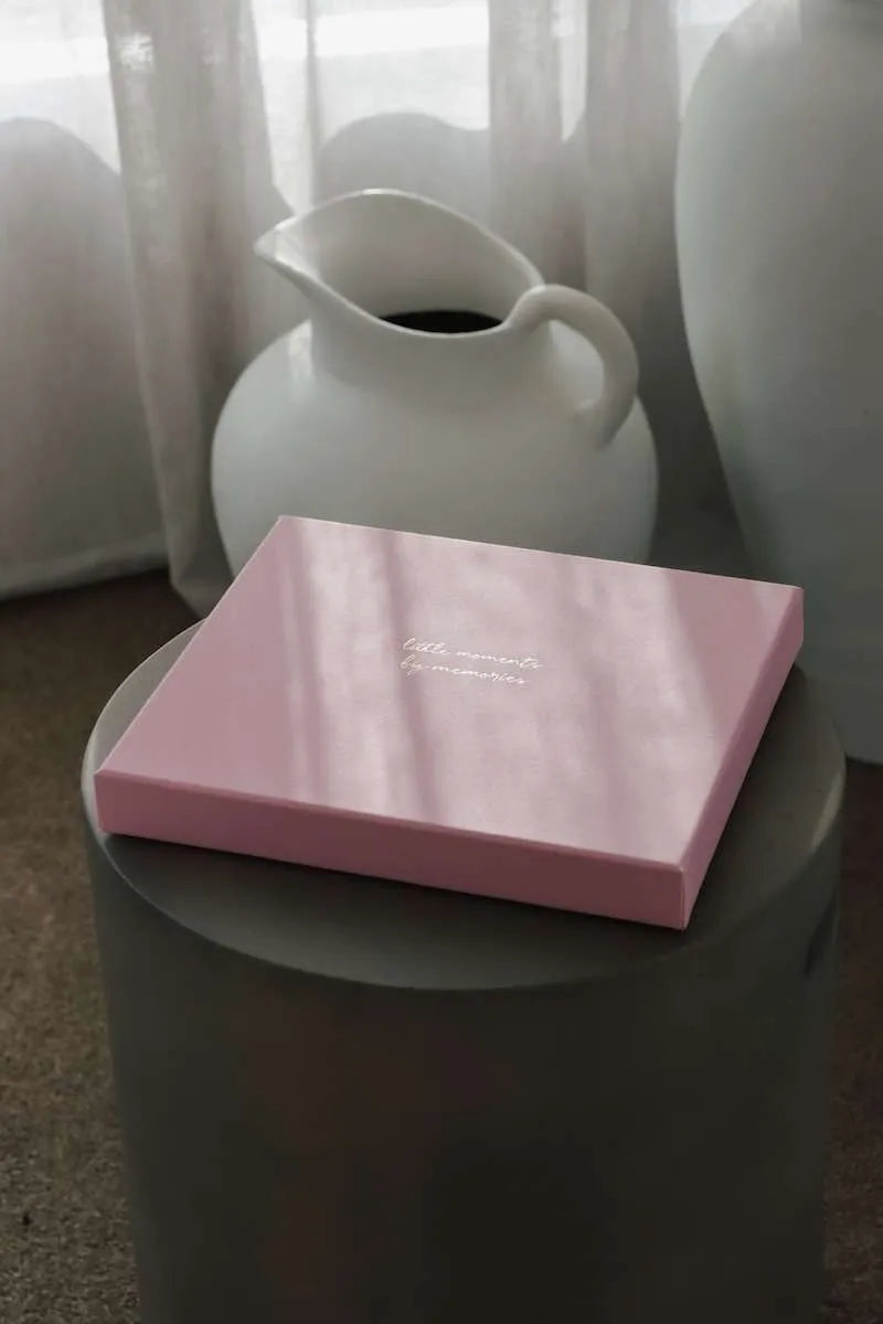 Pink box with text on a gray surface, with white vases in the background