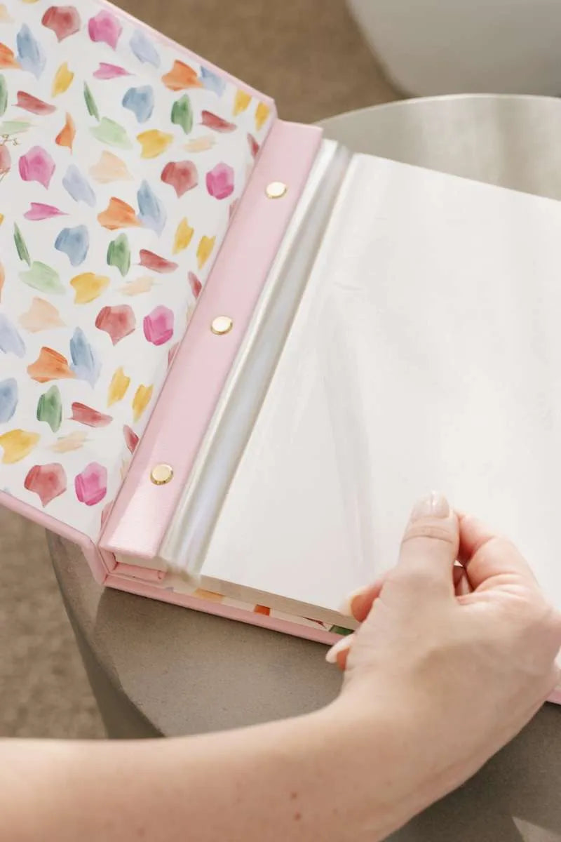 Open photo album with floral cover held by a hand on a neutral background