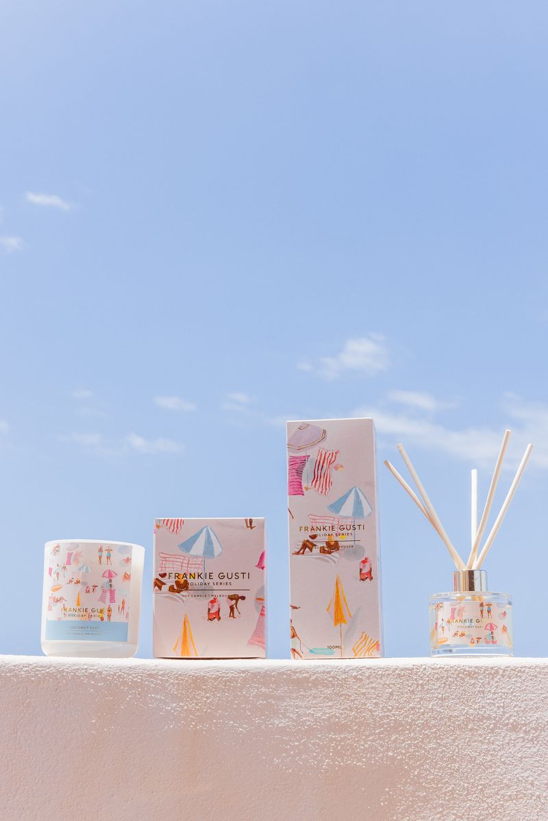 Decorative candles and diffusers with packaging on a textured surface against a blue sky.