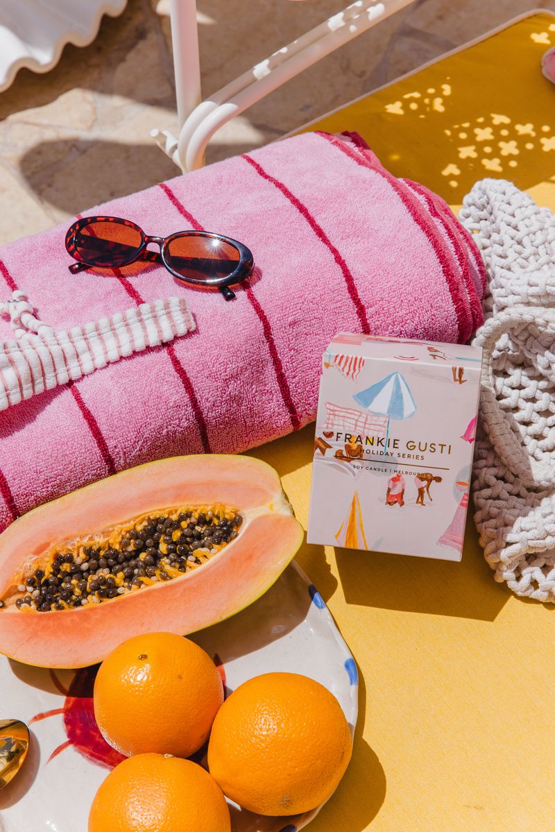 Fruit platter with papaya, oranges, and a box of Frankie Gusti candle on a pink towel.