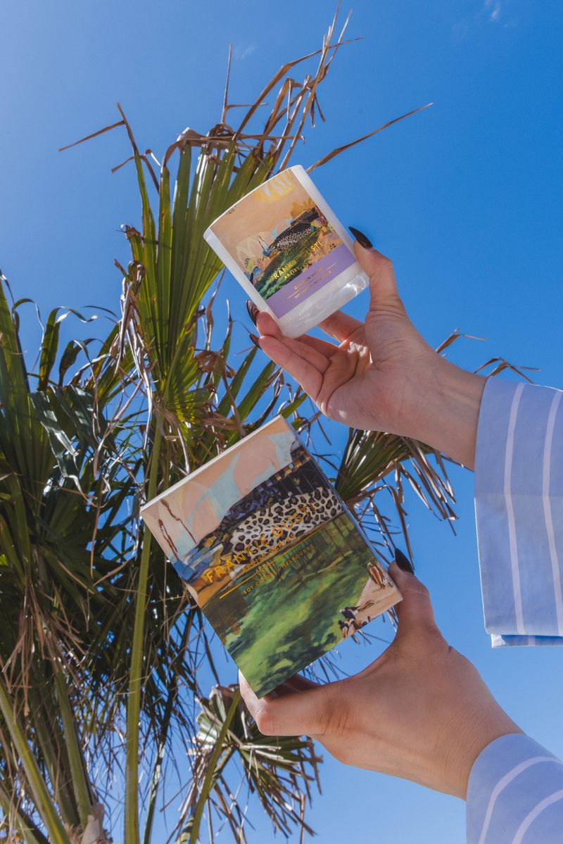 Two hands holding a candle and box with nature scenes against a clear blue sky.