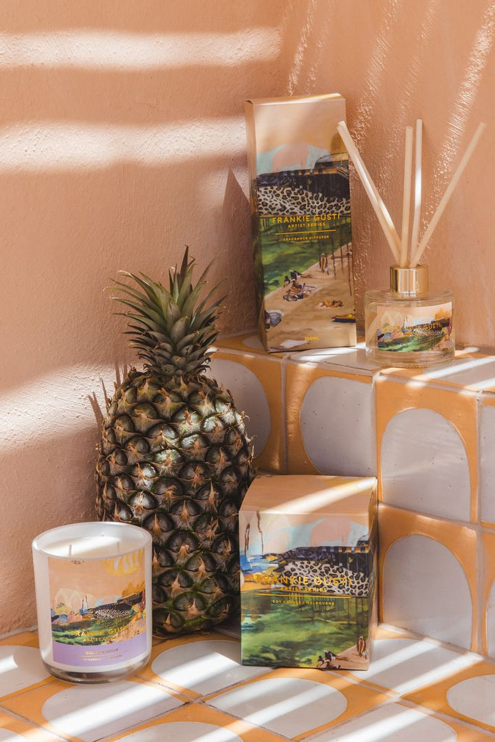 Decorative items including a pineapple, candle, and diffuser on a patterned surface with a warm-toned wall.