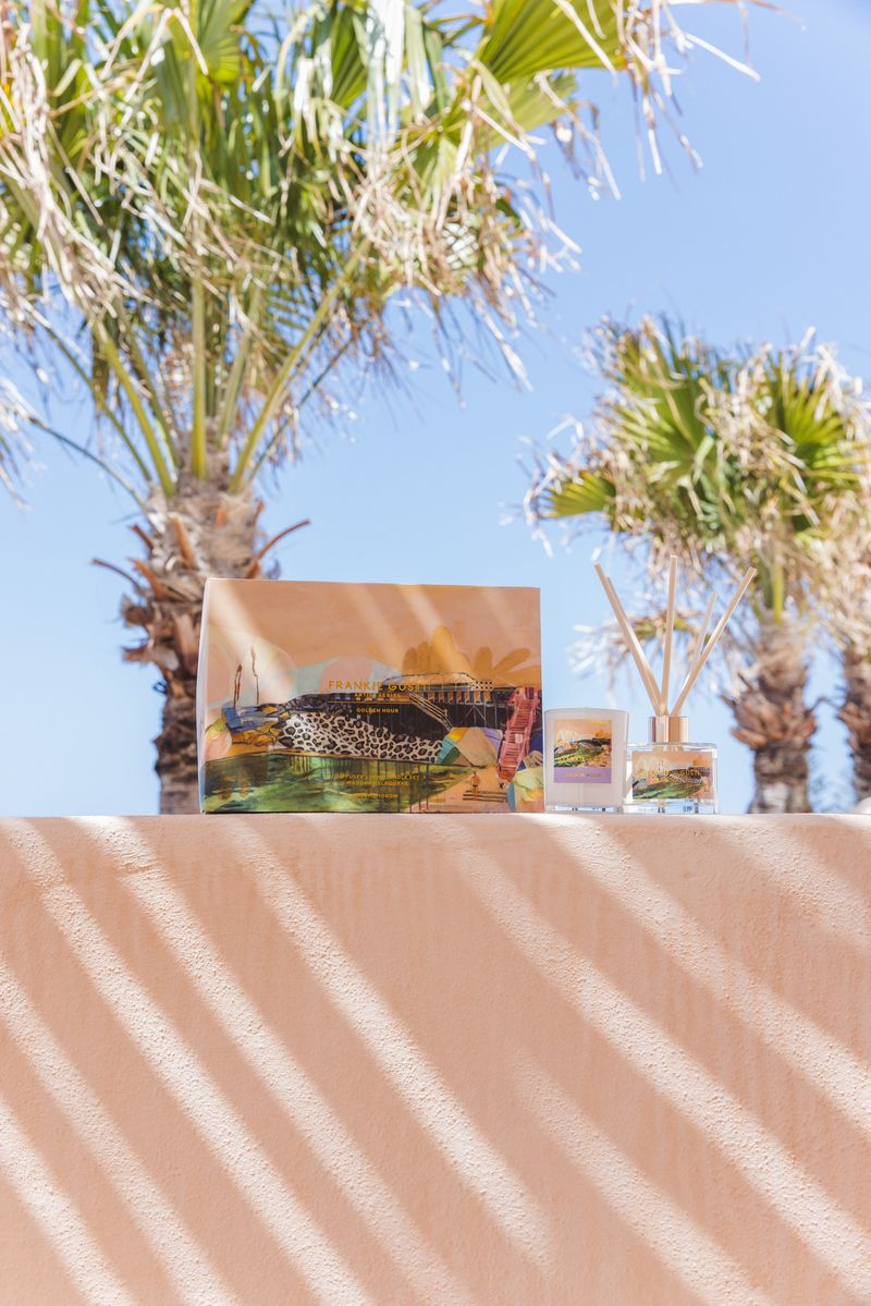 Decorative items including a box, diffuser, and small candle on a textured surface with palm trees in the background.