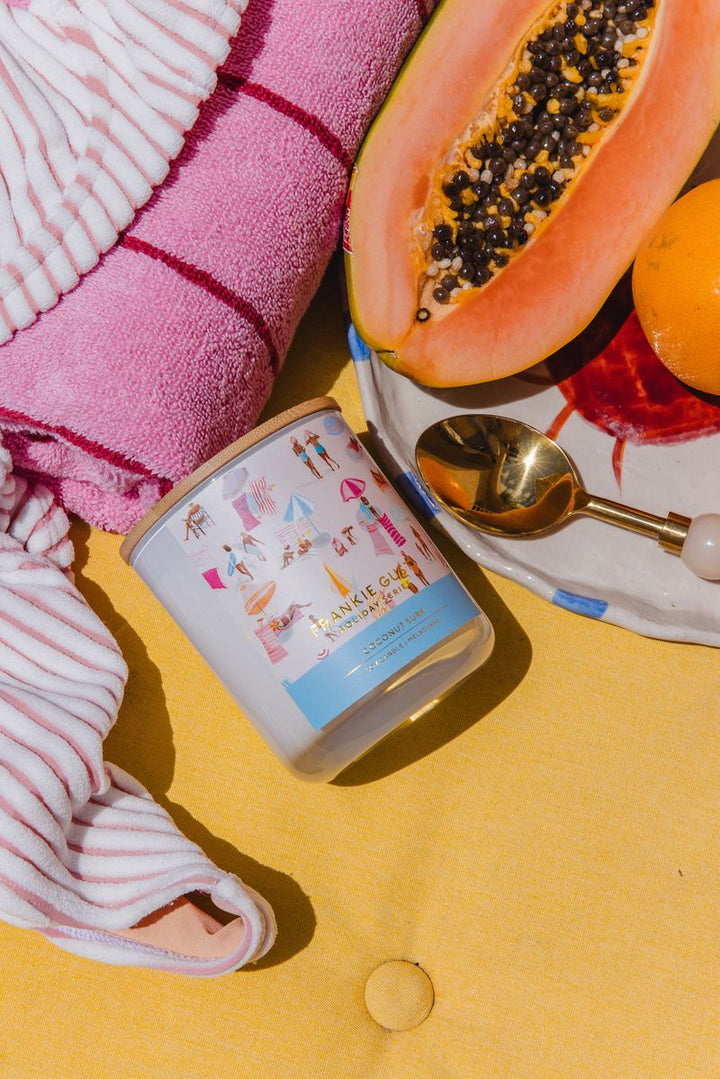 Candle with a label, papaya, and towel on a yellow surface