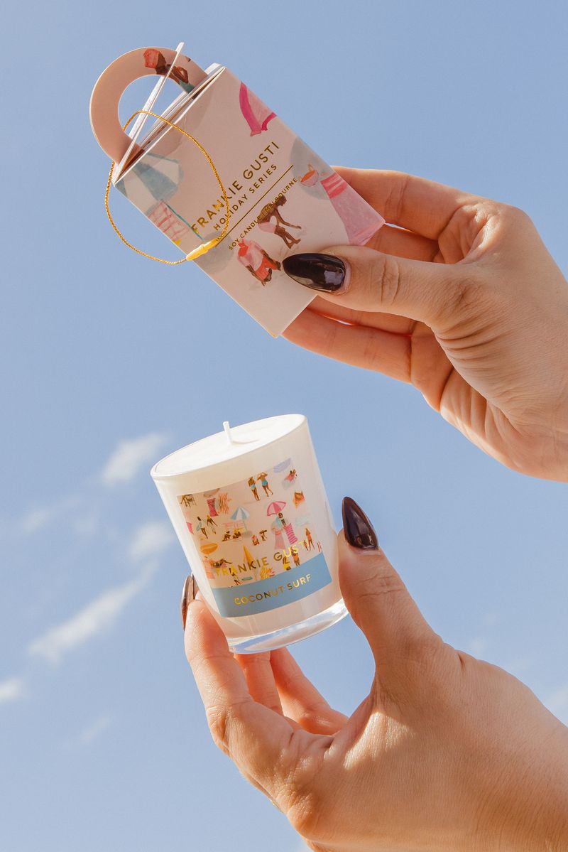 Hand holding a candle with packaging against a clear blue sky