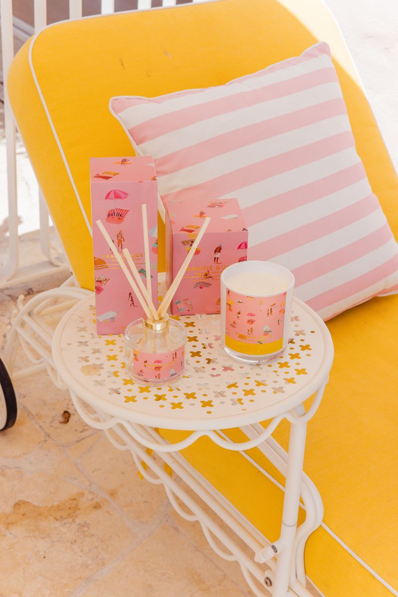 Pink diffuser and candle on a small round table with a yellow chair and striped pillow in the background.