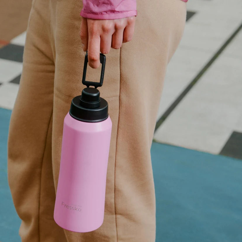 Person holding a pink water bottle with a black cap on a checkered floor.