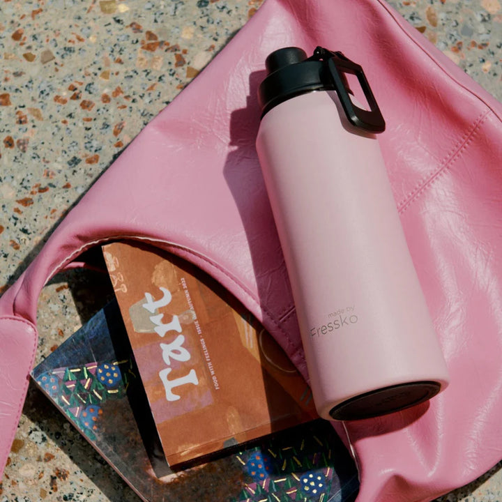 Pink water bottle on a pink bag with a phone and magazine underneath