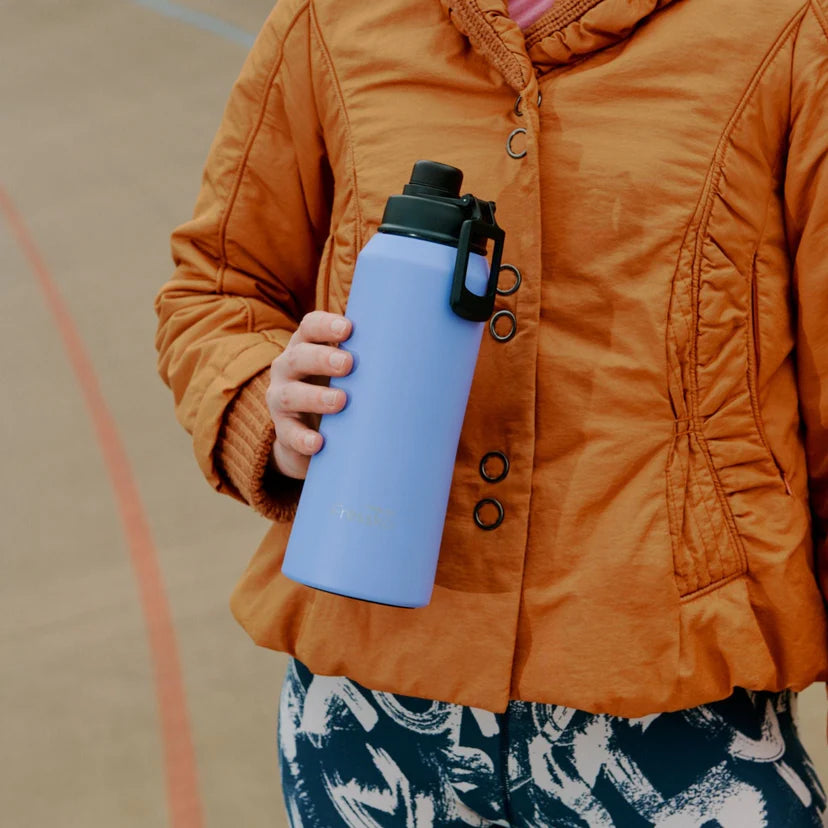 Person wearing an orange jacket holding a blue water bottle on a basketball court.