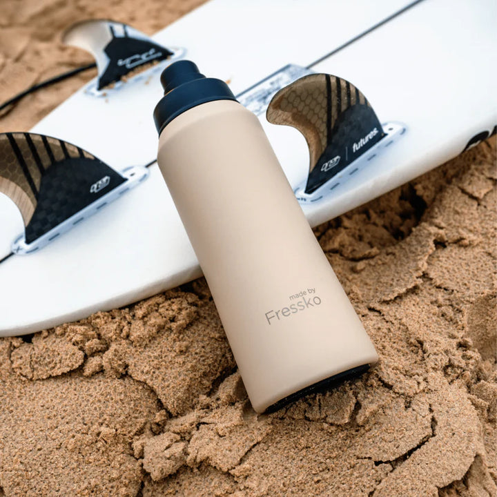 Beige water bottle with black cap on a surfboard in the sand