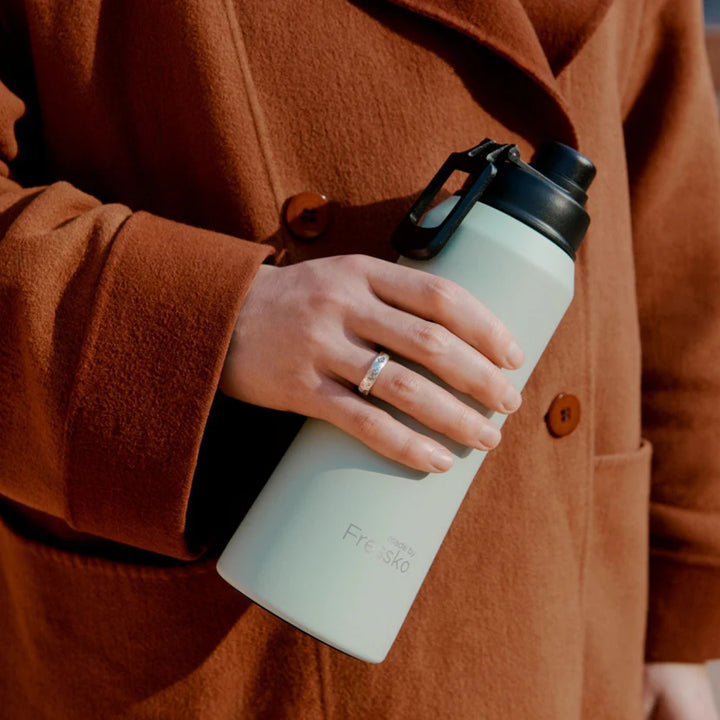 Person holding a light-colored water bottle with a black lid, wearing a brown coat.