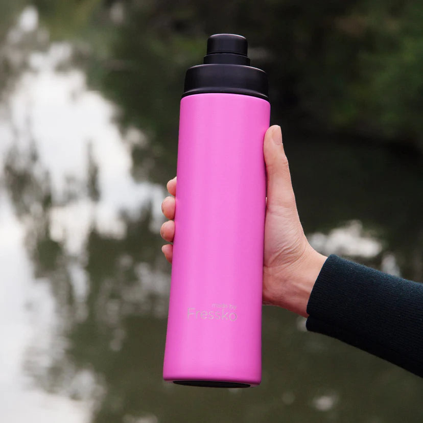 Hand holding a pink water bottle with a black cap against a blurred natural background