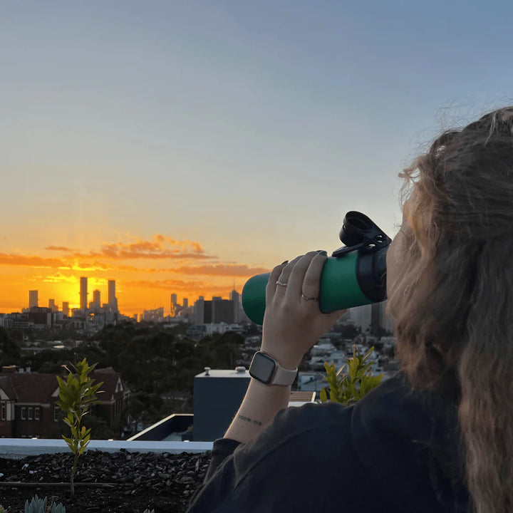 Person using binoculars to look at a cityscape during sunset