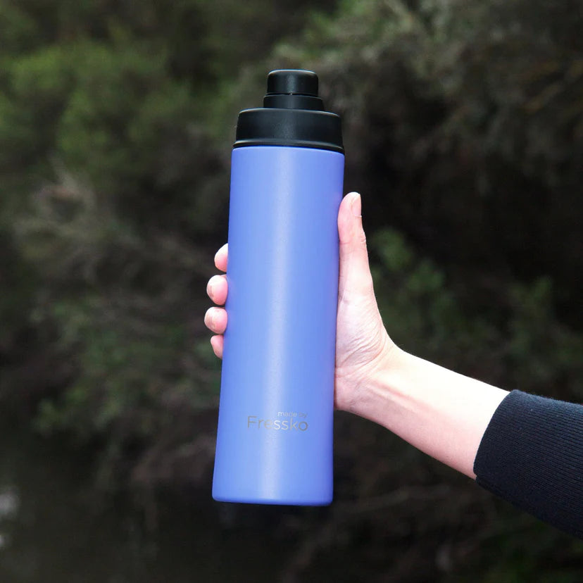 Hand holding a blue water bottle with black cap against a blurred natural background