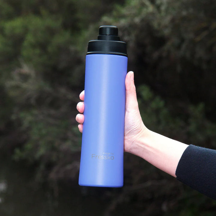 Hand holding a blue water bottle with black cap against a blurred natural background