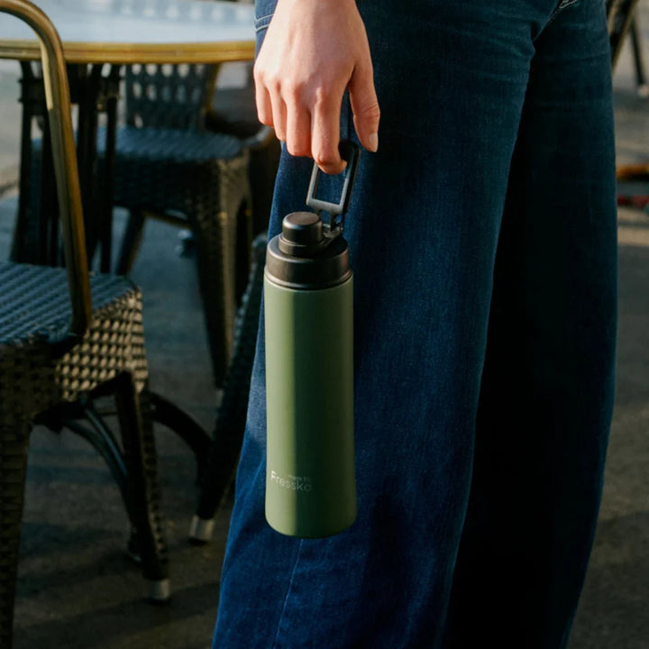 Person holding a green insulated bottle with a blurred outdoor background