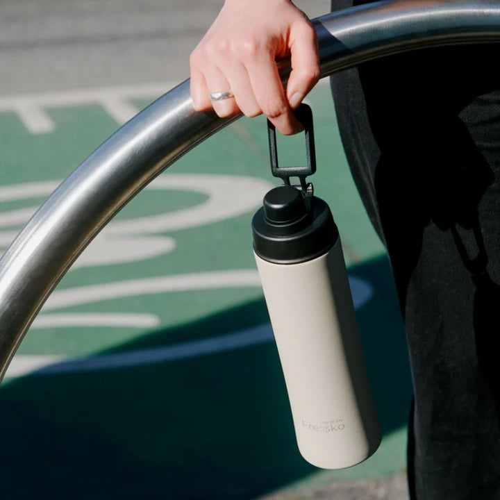 Person holding a beige water bottle with a black cap on a metal railing.