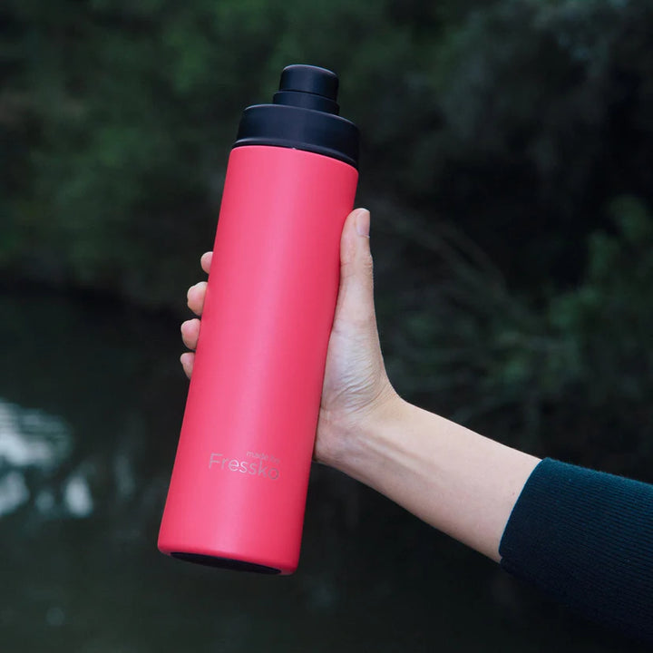 Hand holding a pink water bottle with a black cap against a blurred natural background