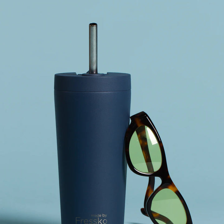 Blue tumbler with a straw and sunglasses on a light blue background