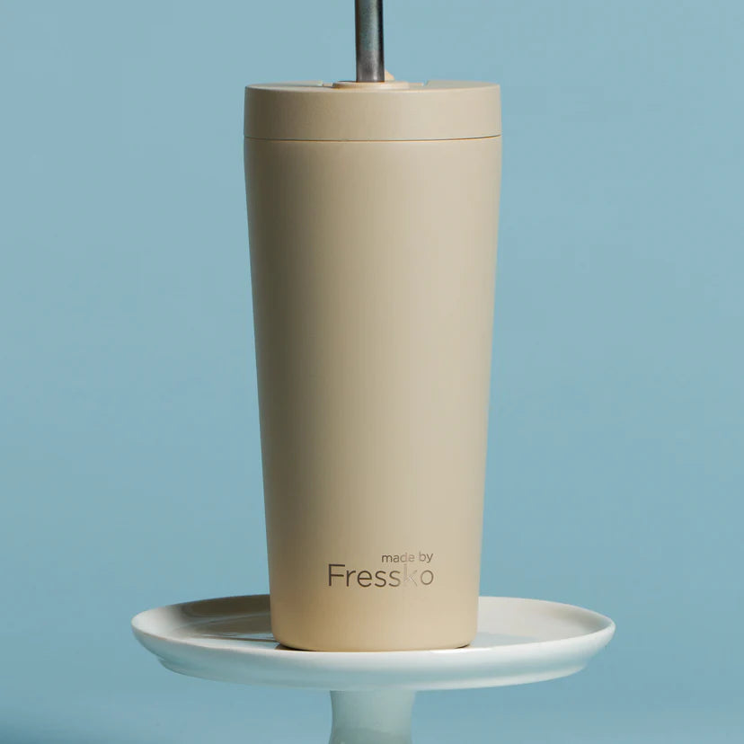 Beige tumbler with a straw on a white stand against a blue background