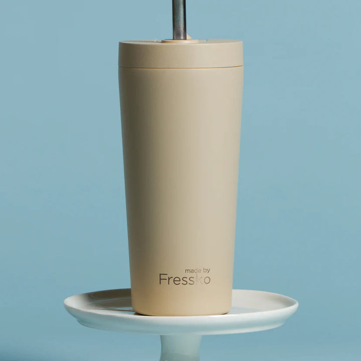 Beige tumbler with a straw on a white stand against a blue background