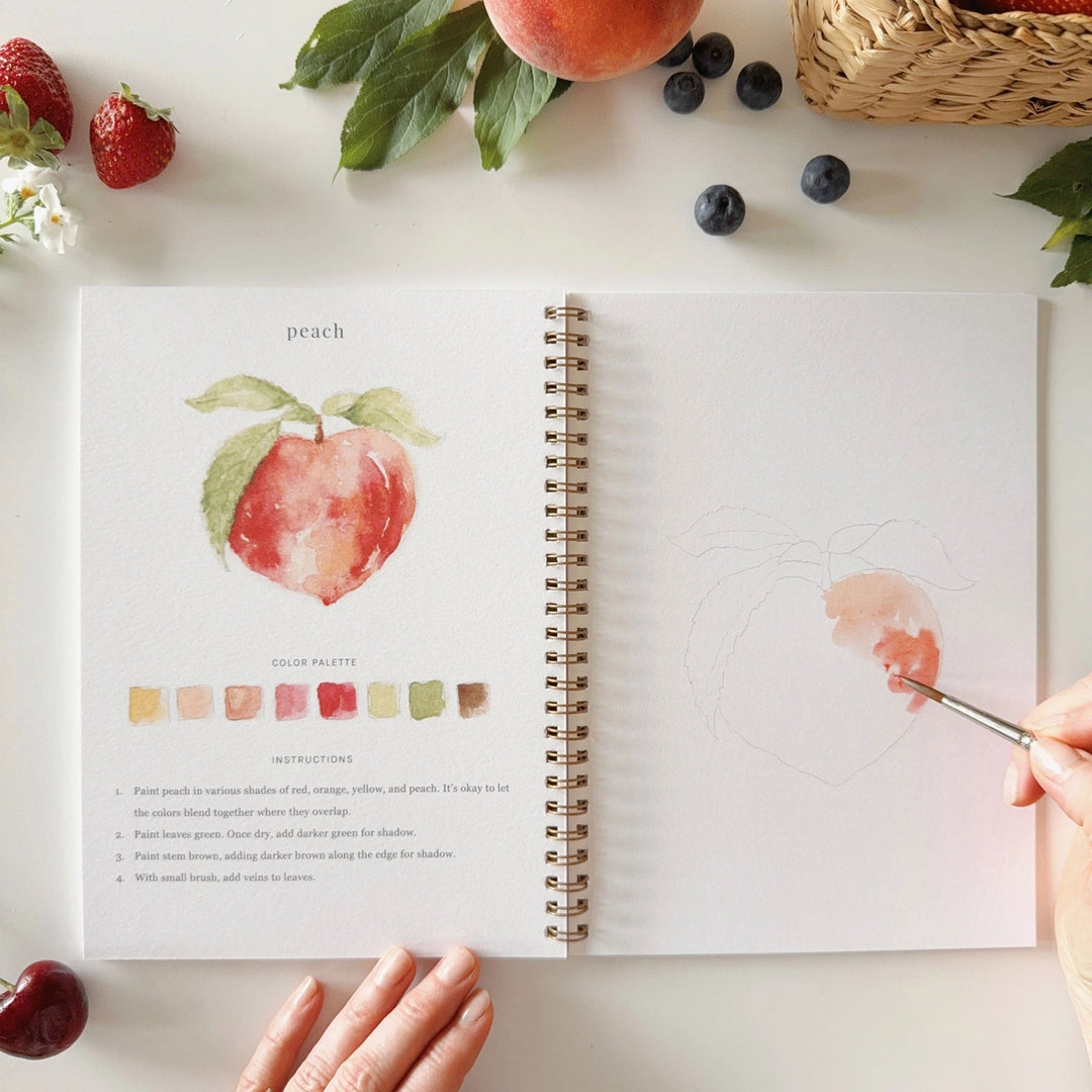 Open book with a peach illustration and color swatches on a table with fruits around