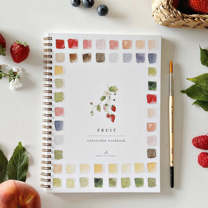 Watercolor workbook titled 'Fruit' with a brush and fruits on a white surface