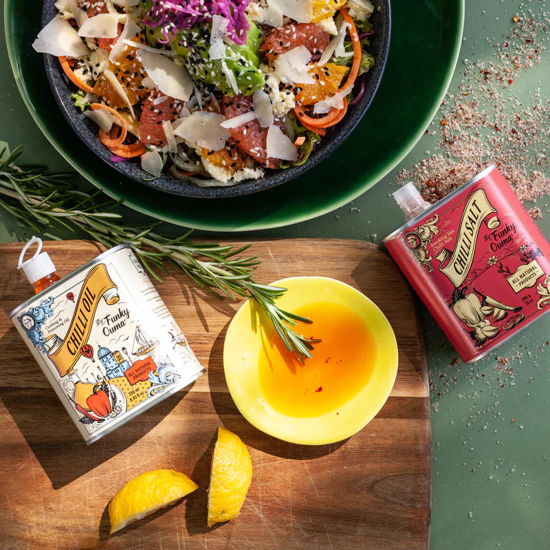 Chili oil bottles with a bowl of salad and lemon on a wooden cutting board.