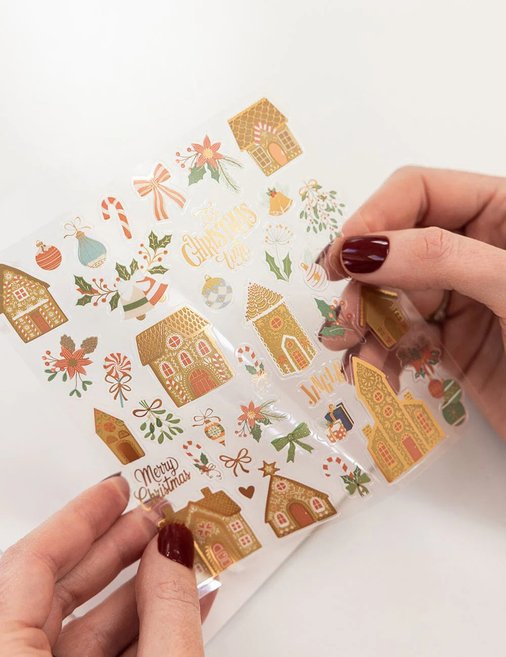 Sheet of Christmas-themed stickers with gingerbread houses and decorative elements held by a person.