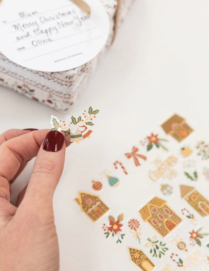 Hand holding a sheet of decorative stickers with gingerbread houses and other festive designs.