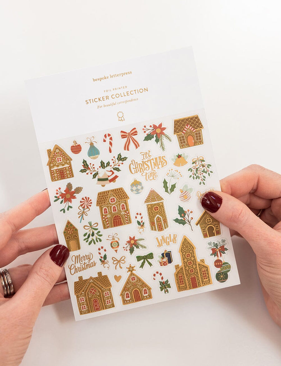 Sheet of Christmas-themed stickers held by hands with a white background