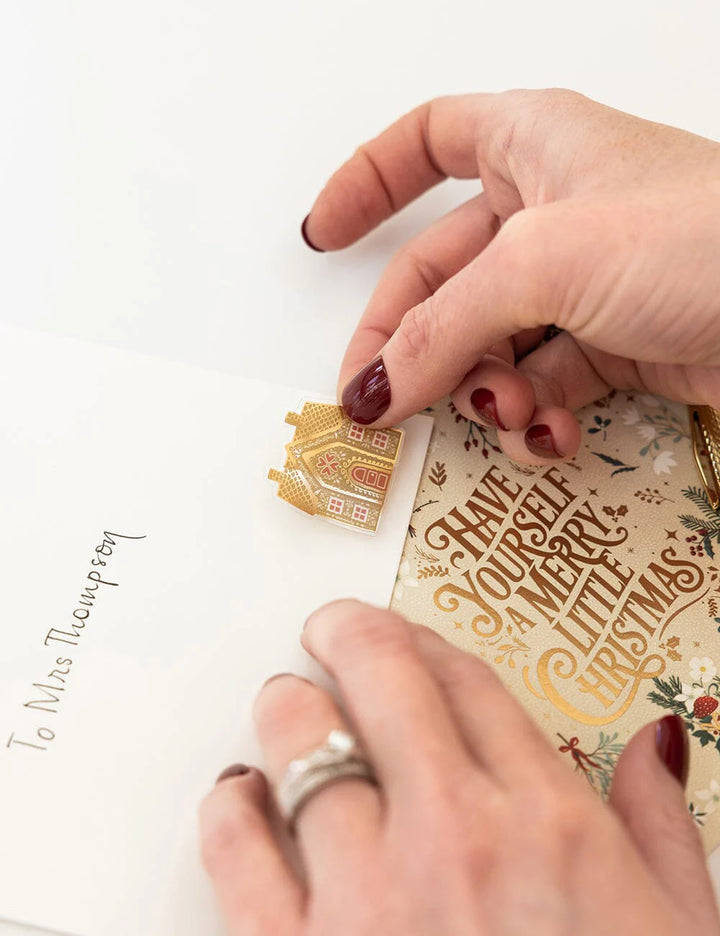 Hand holding a small gold ornament with intricate designs on a Christmas card.
