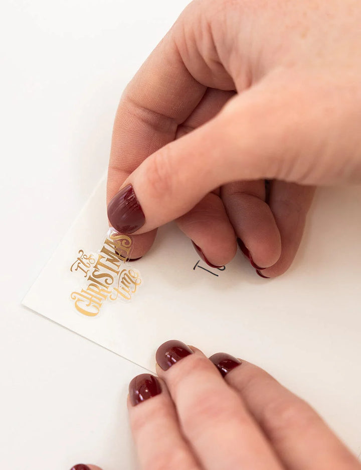 Close-up of hands with maroon nail polish holding a card with gold text.