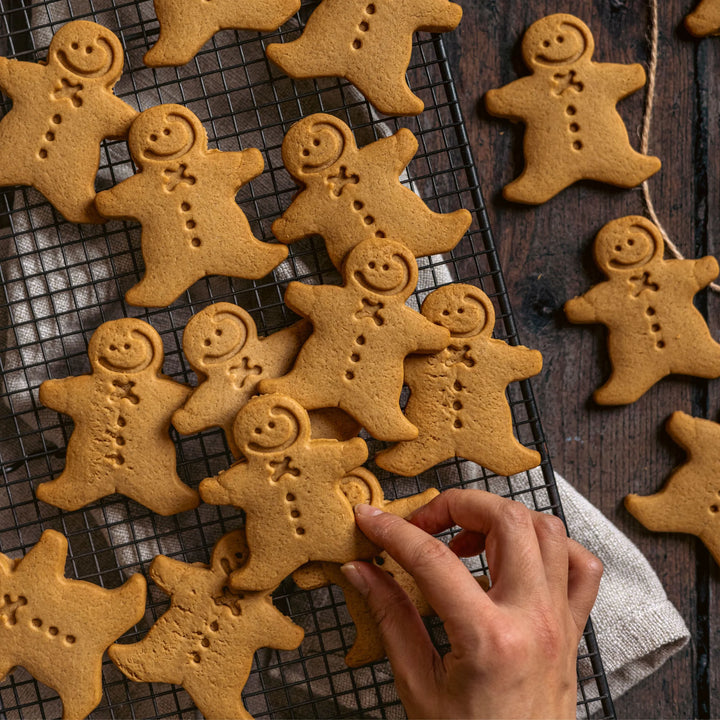 Baked gingerbread men on a cooling rack with a hand reaching out to touch one.