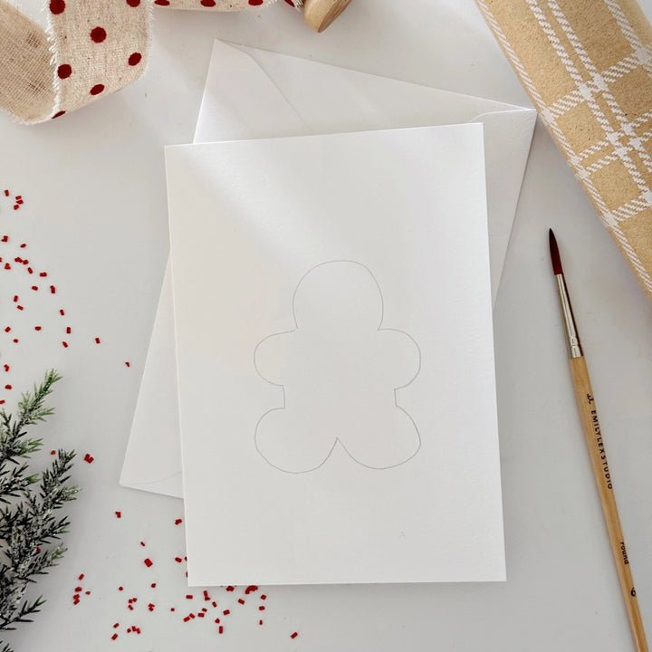 White card with a gingerbread man cutout on a white surface with decorative items.