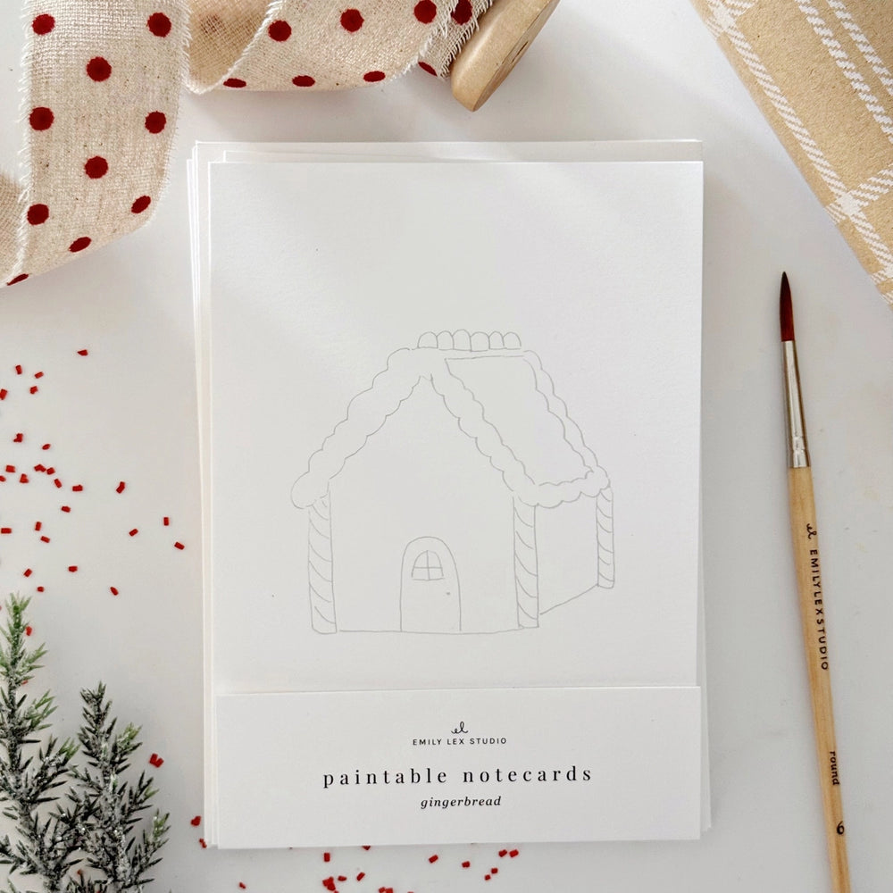 Paintable notecard with gingerbread house design on a white surface with decorative elements.
