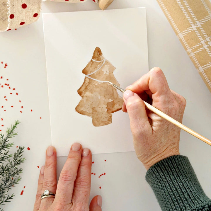 Person painting a Christmas tree on a card.