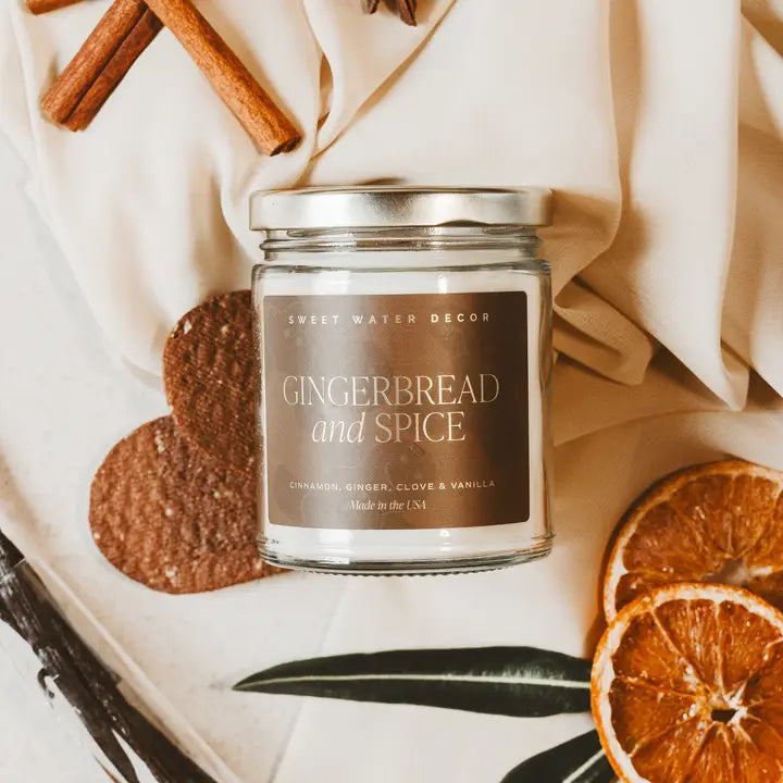 Candle jar labeled 'Gingerbread and Spice' with cinnamon sticks, cookies, and oranges on a neutral background